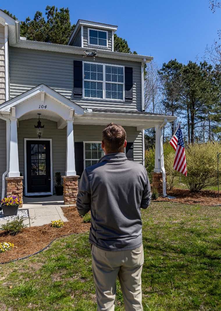 A man is standing in front of a house with an american flag.