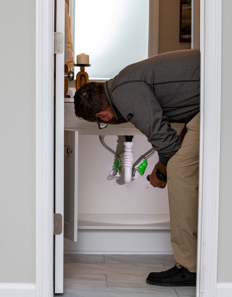 A man is looking under a sink in a bathroom
