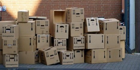 Stacked cardboard shipping boxes against a brick wall in an outdoor loading area