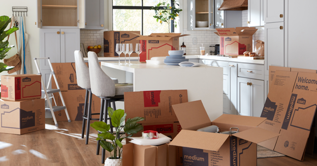 Bright kitchen with many moving boxes and open cardboard cartons, suggesting a recent move or unpacking