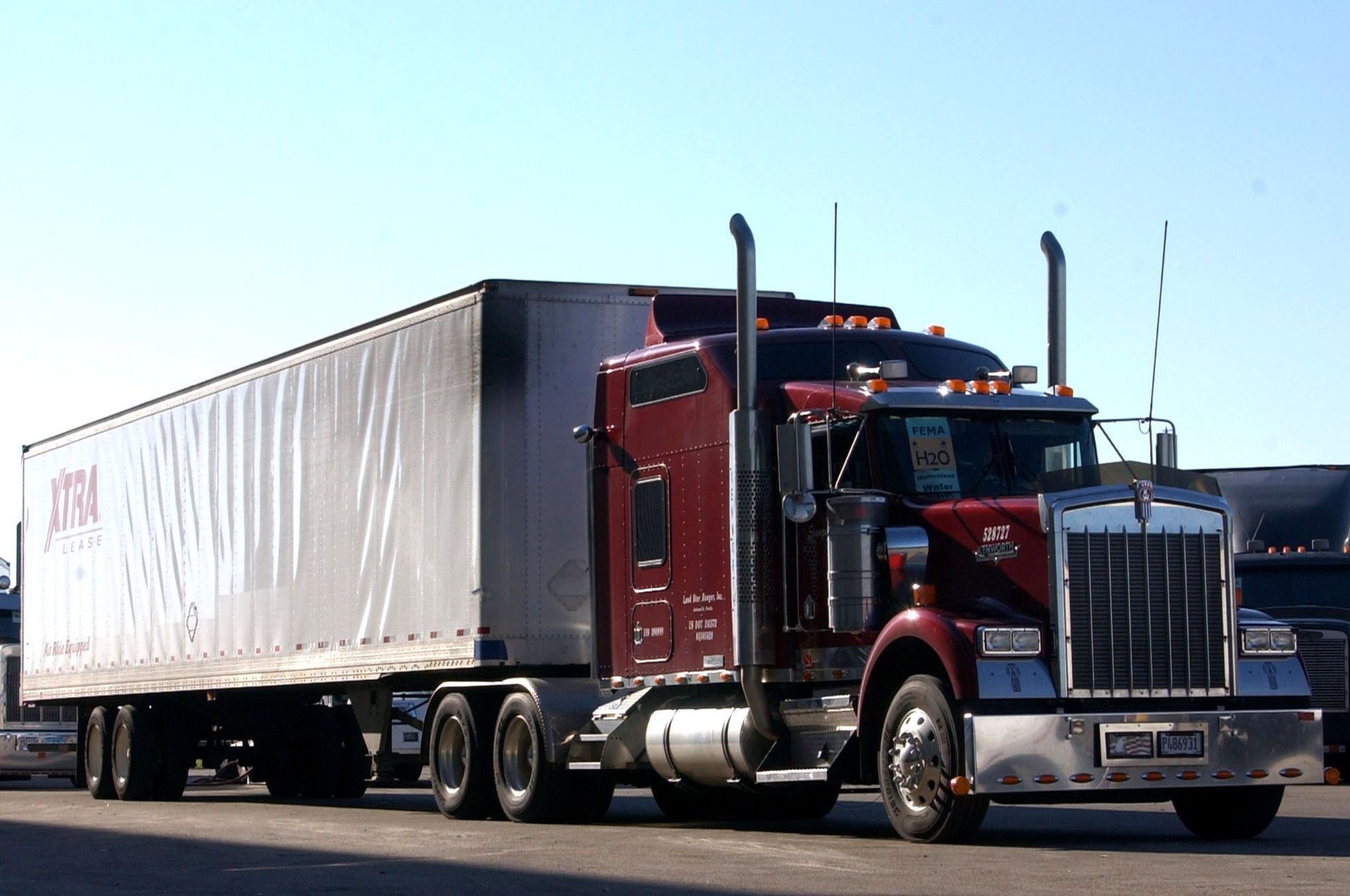 Red semi-truck hauling a white trailer on a highway under a clear blue sky