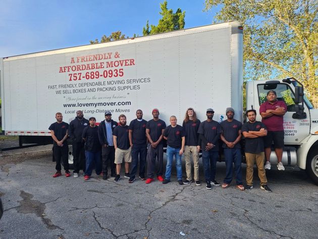 Group of workers posing in front of a white moving truck on a sunny street.