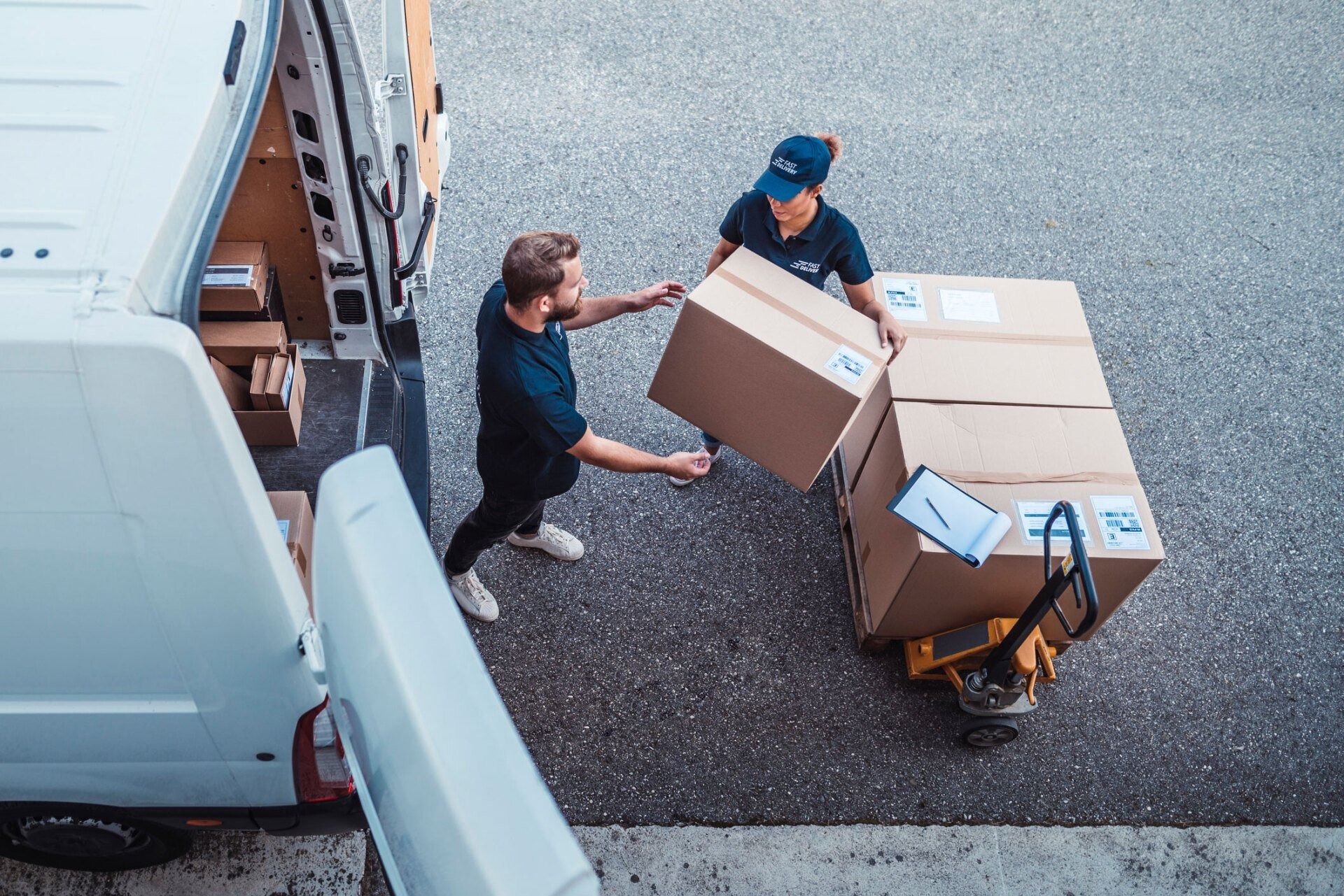 Two movers loading cardboard boxes from a truck onto a handcart in a parking lot