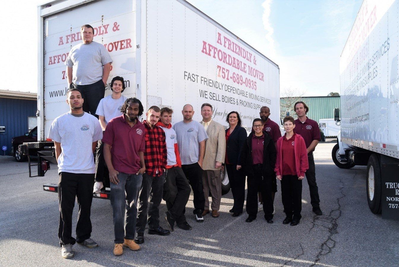 Group of volunteers posing between two moving trucks in a parking lot, some standing on the truck and on the ground.