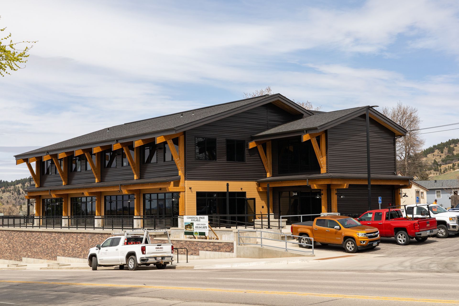 Two-story building with dark wood siding, light wood trim. Several trucks parked outside.