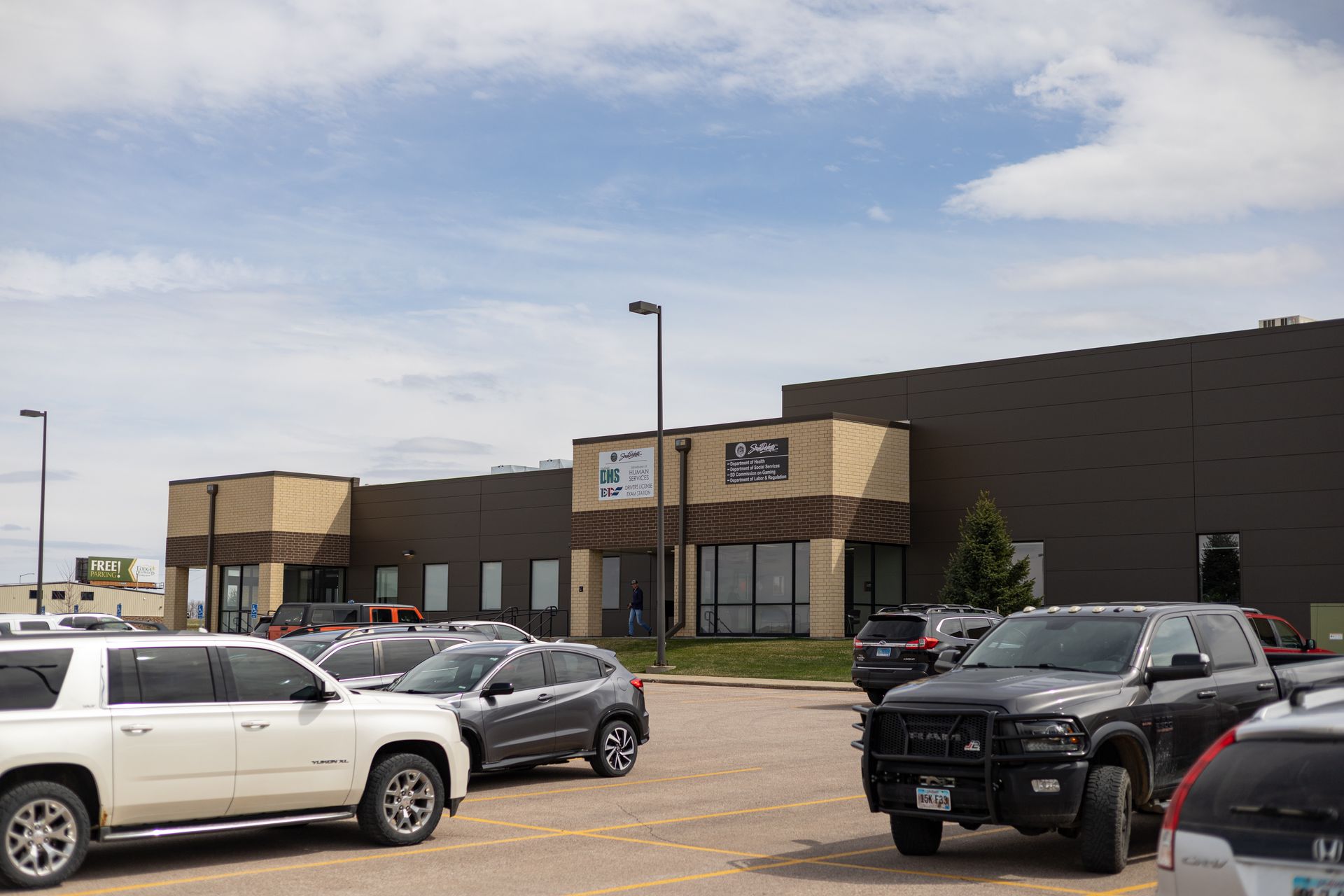 Building with parking lot; various vehicles parked in front of a modern structure with blue sky in background.