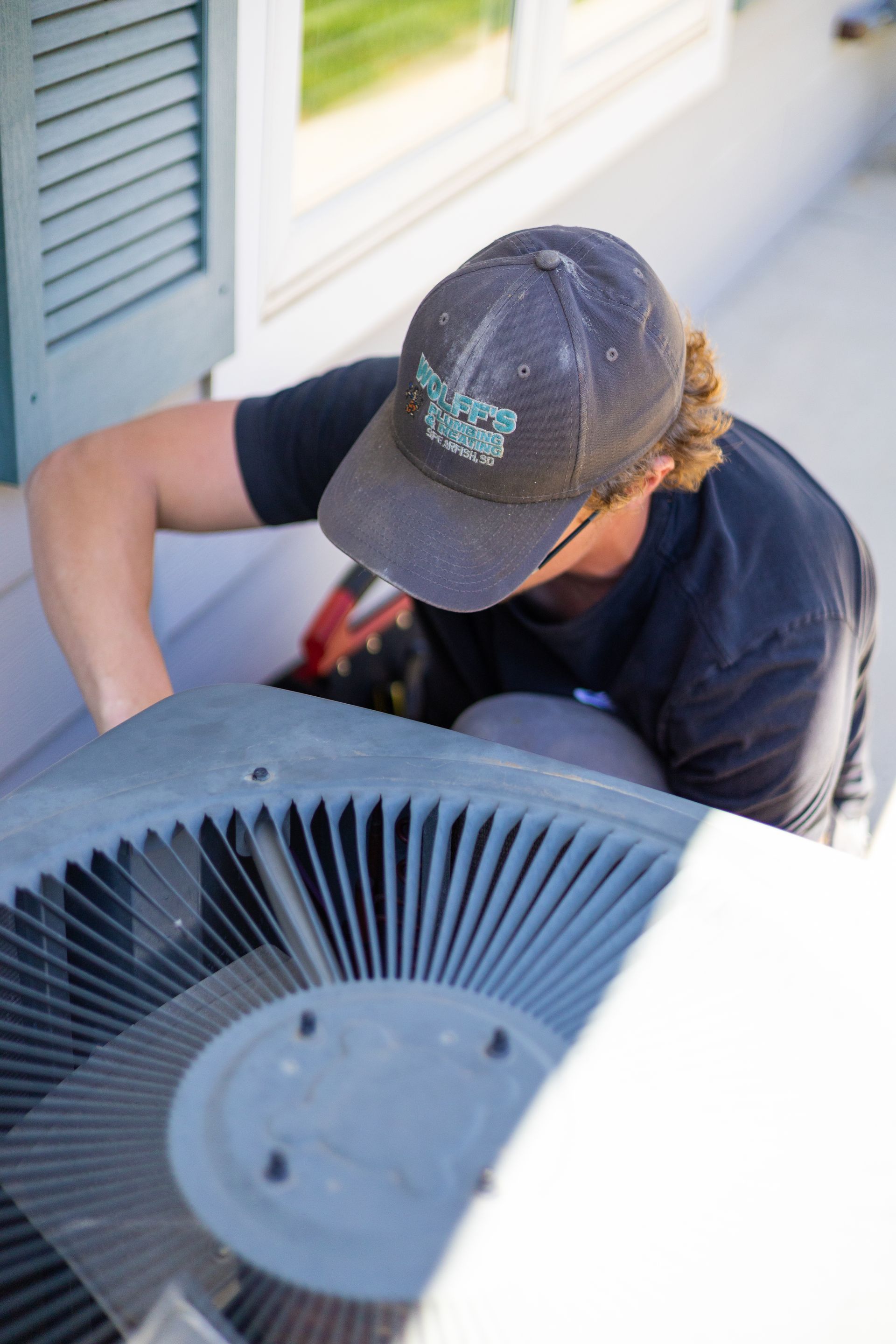 HVAC technician working on an air conditioning unit outside a house.