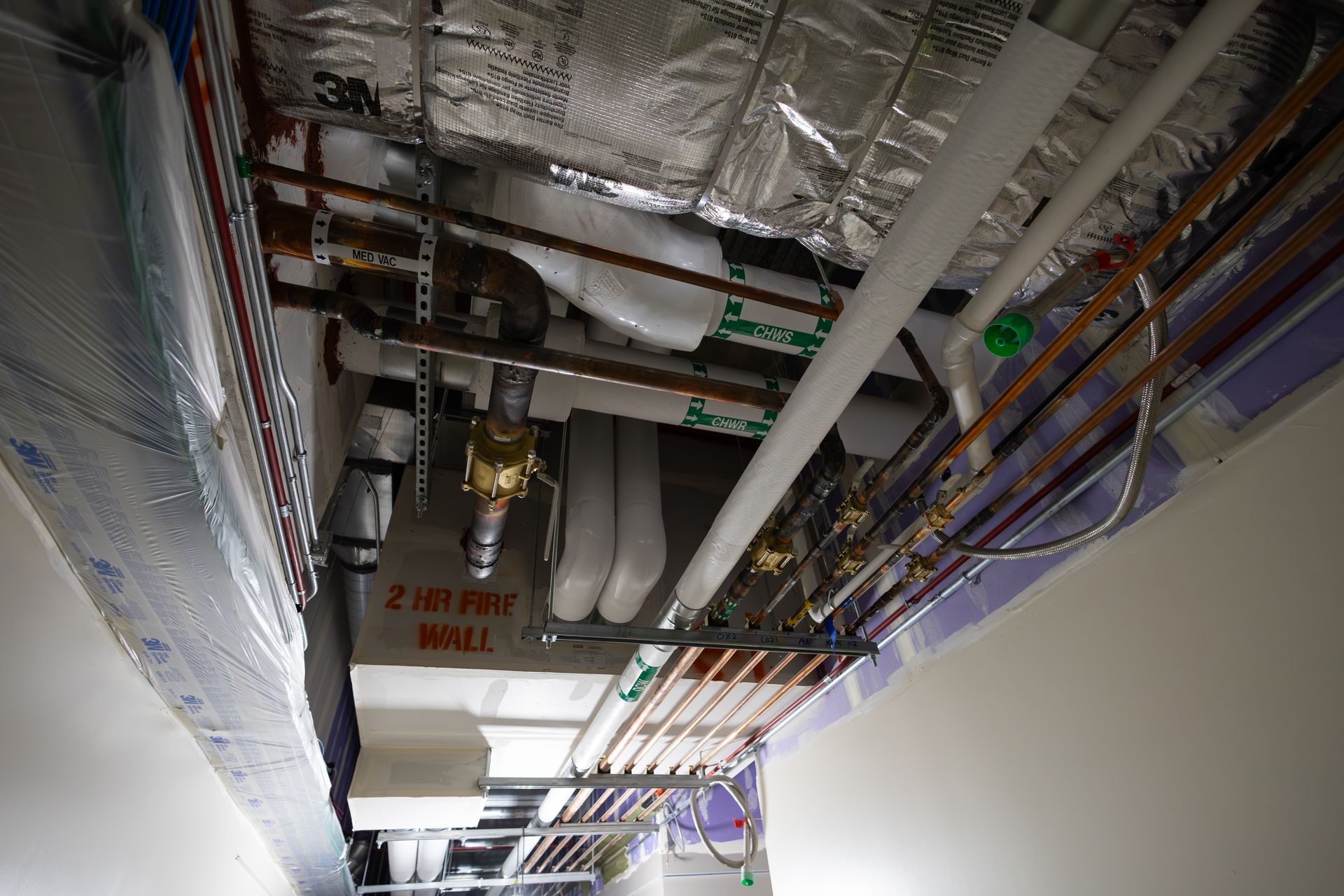 Pipes and ductwork in a building's ceiling, including insulation and exposed copper pipes.
