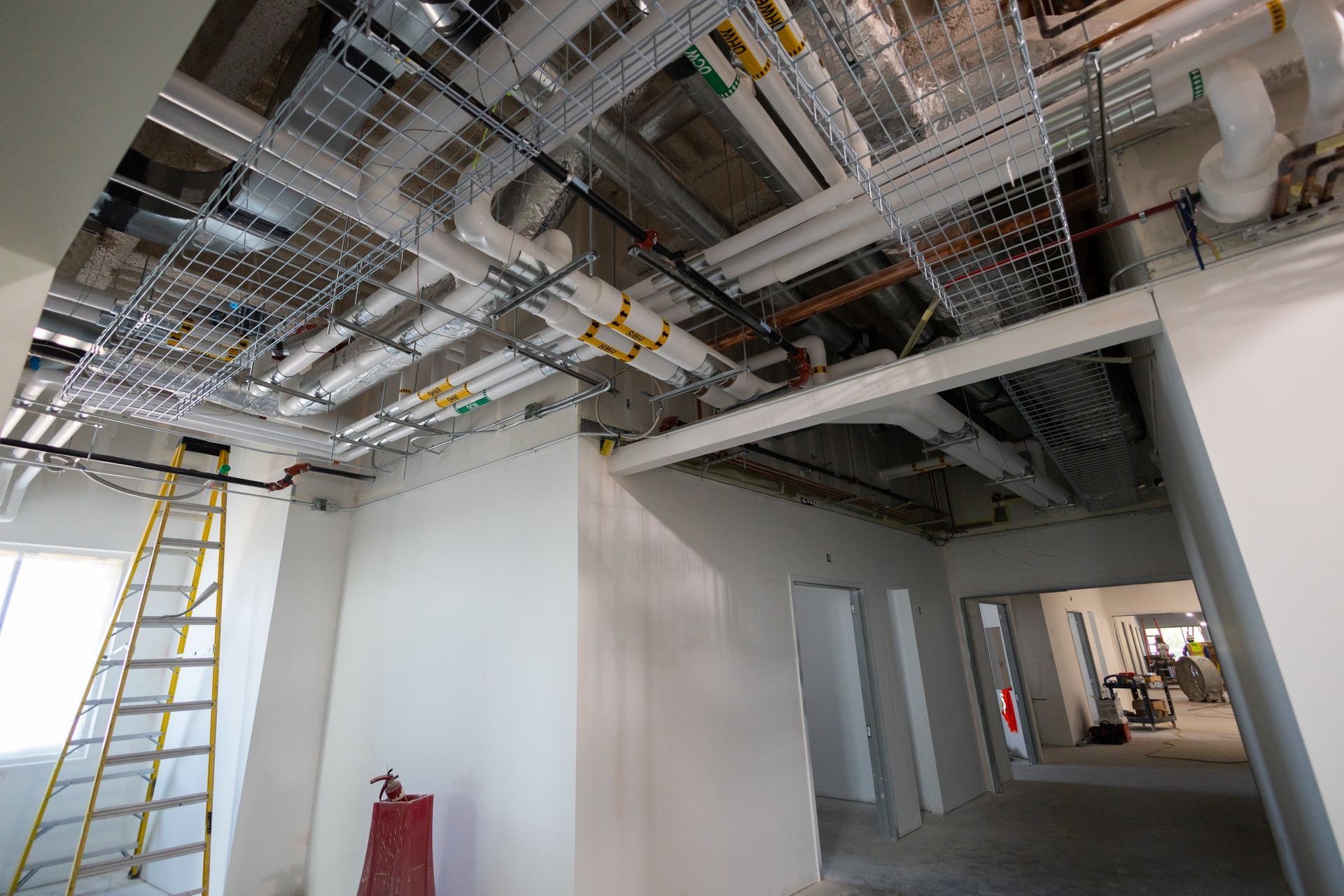Interior of a building under construction, showing exposed wiring and piping on the ceiling.