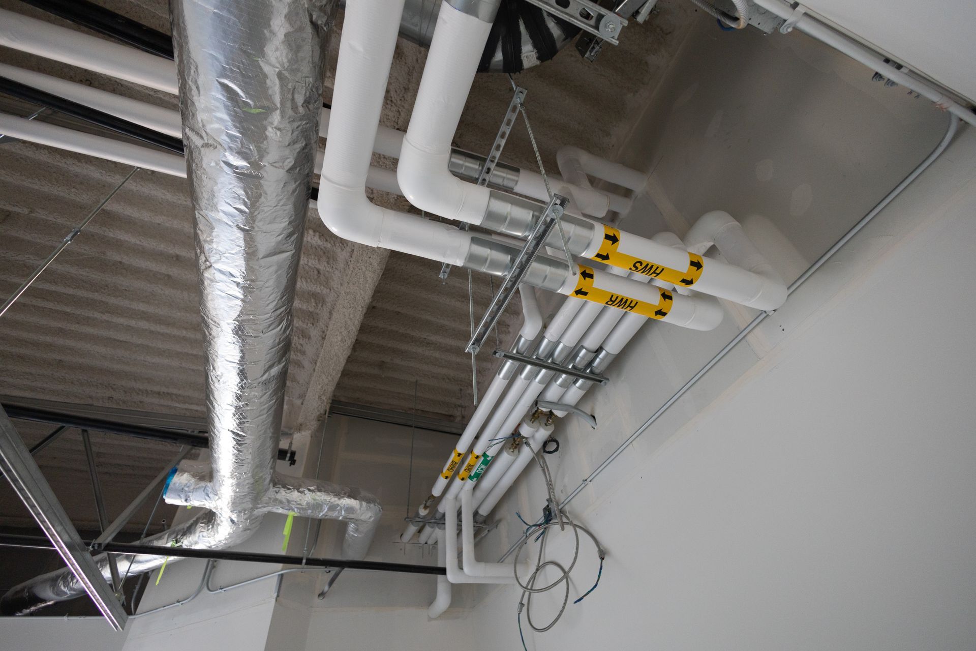 Pipes with white insulation and yellow tags run across a ceiling. Ductwork is also present.