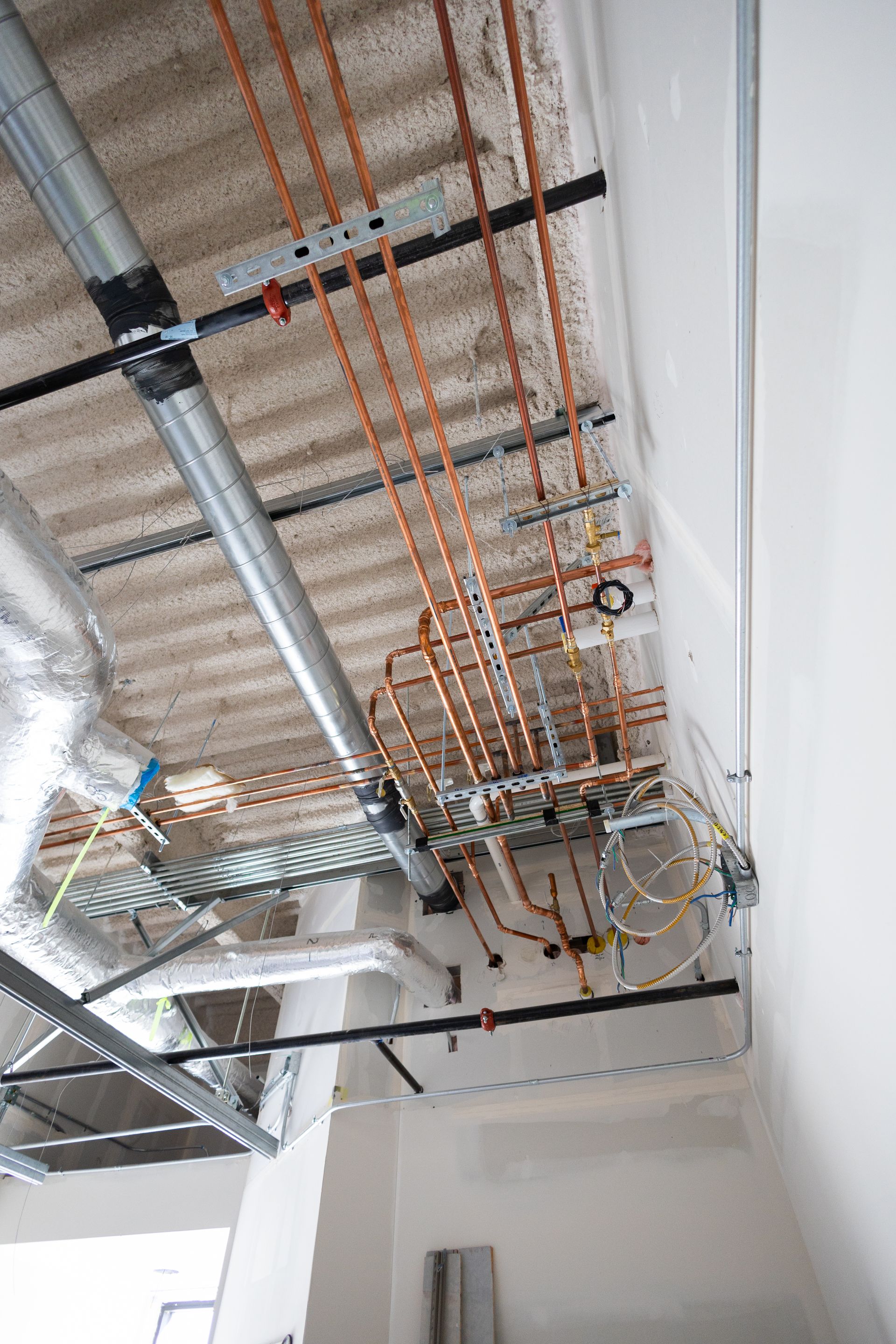 Copper pipes and ductwork installed on a construction ceiling.
