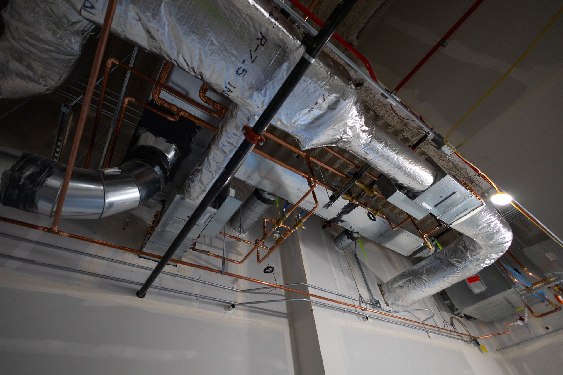 HVAC ductwork and copper piping installed on a ceiling during construction.