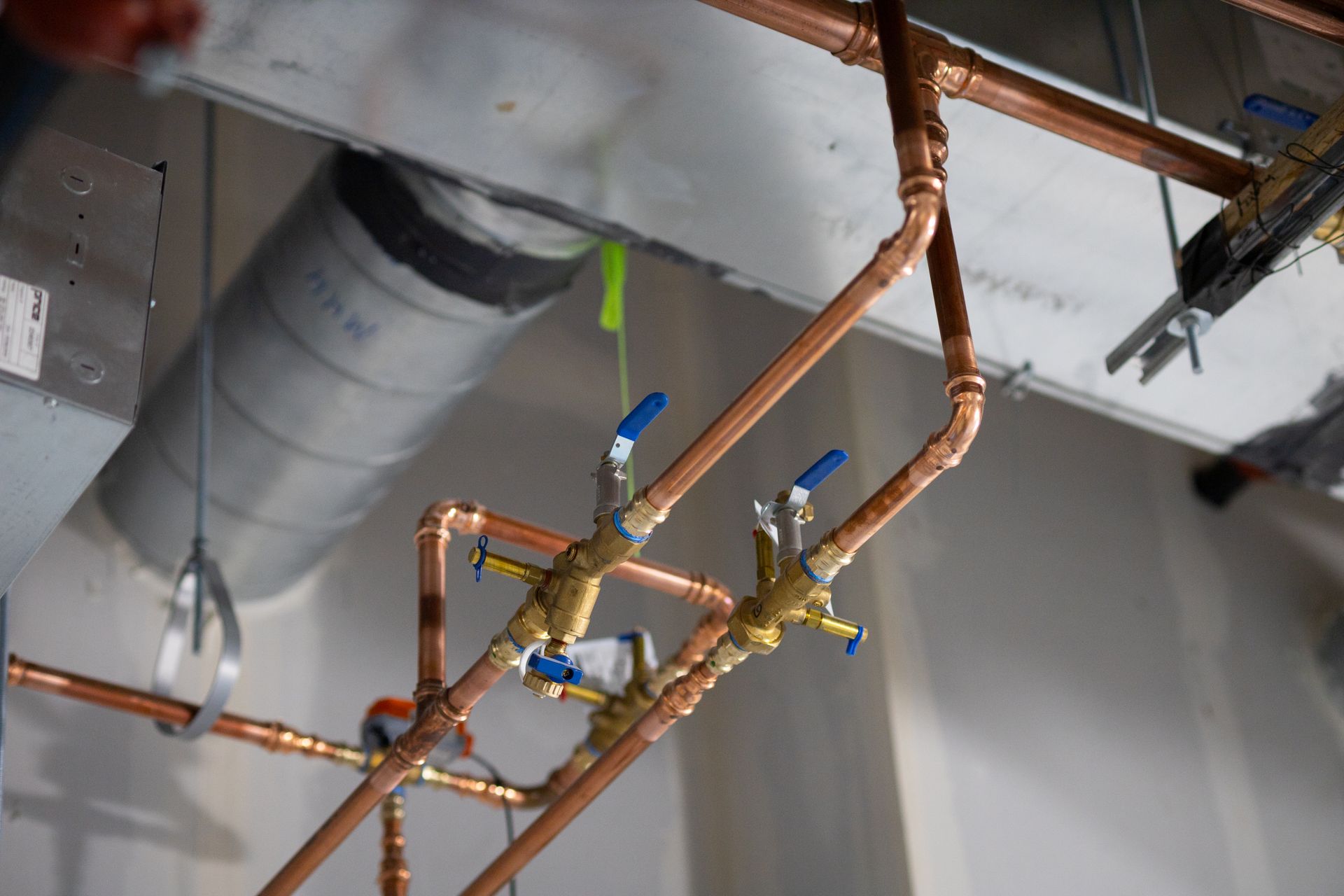 Copper pipes with blue-handled valves installed against a white wall and ceiling; ductwork visible.
