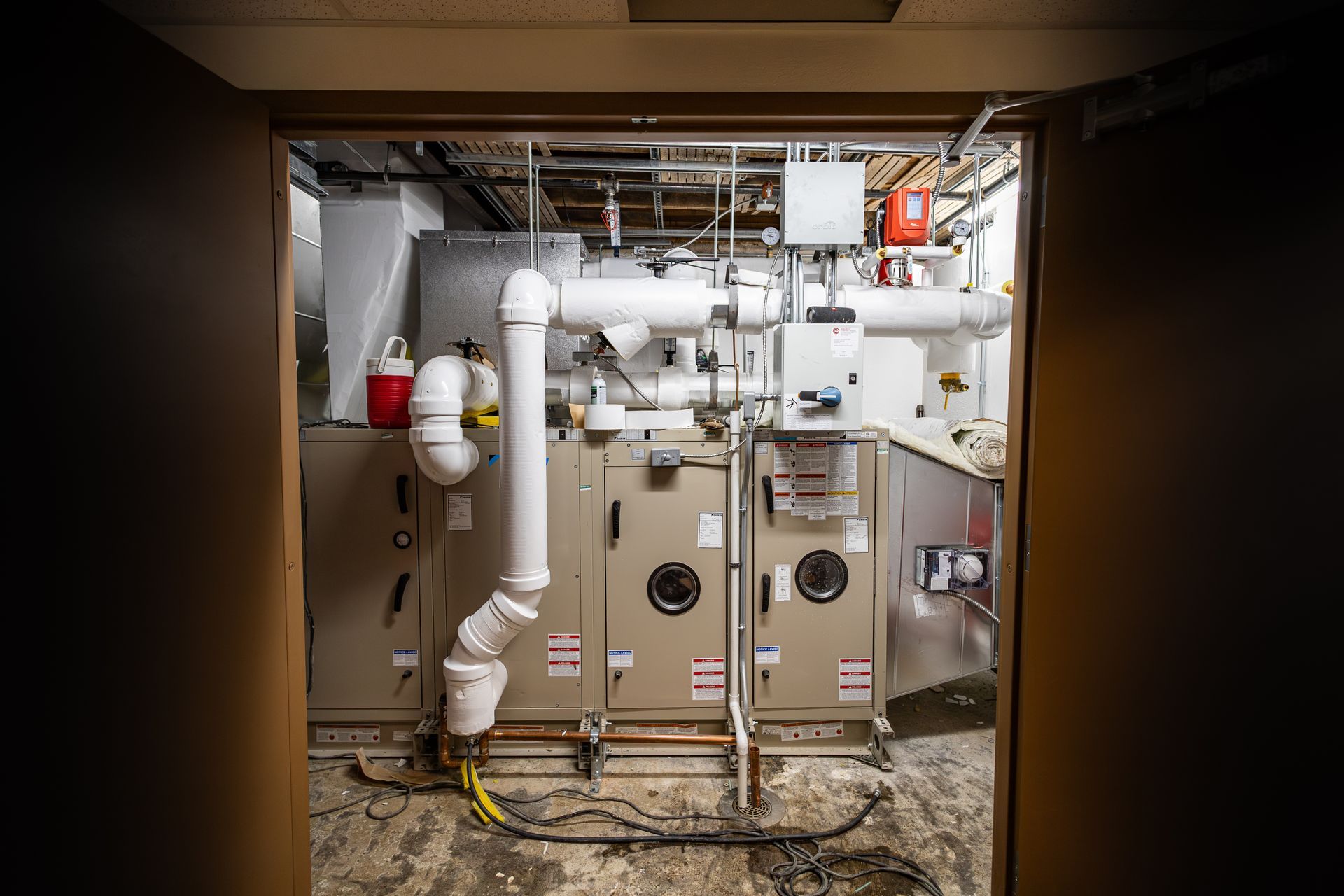 HVAC system in a room. Large machinery with white pipes, beige panels, and a red fire extinguisher.