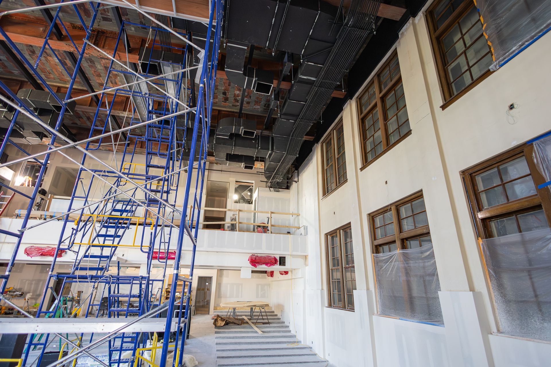 Interior of a building under construction, scaffolding, windows, exposed ceiling, and white walls.