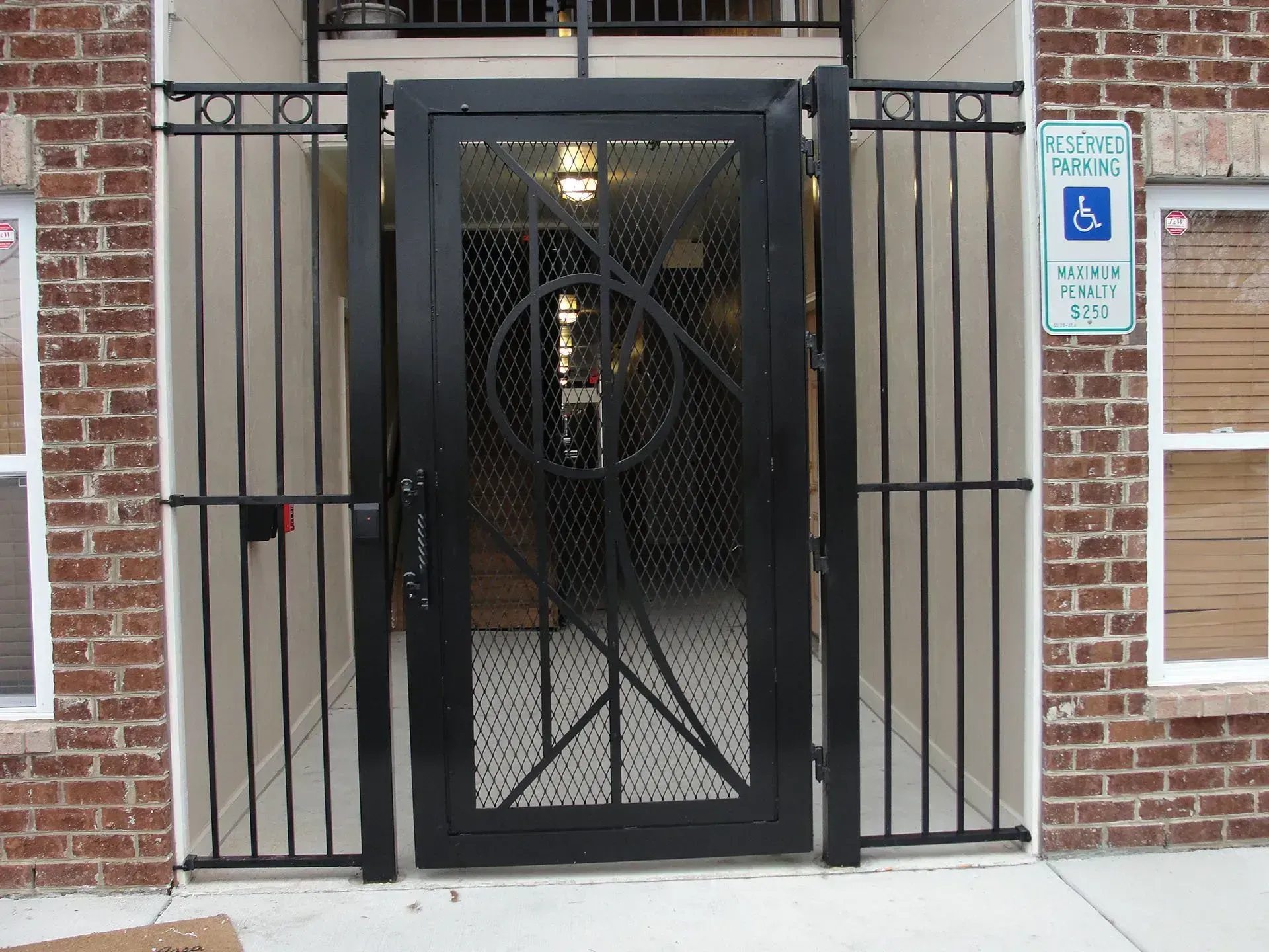 Black metal security gate with side railings in front of a brick building. Handicap parking sign visible.