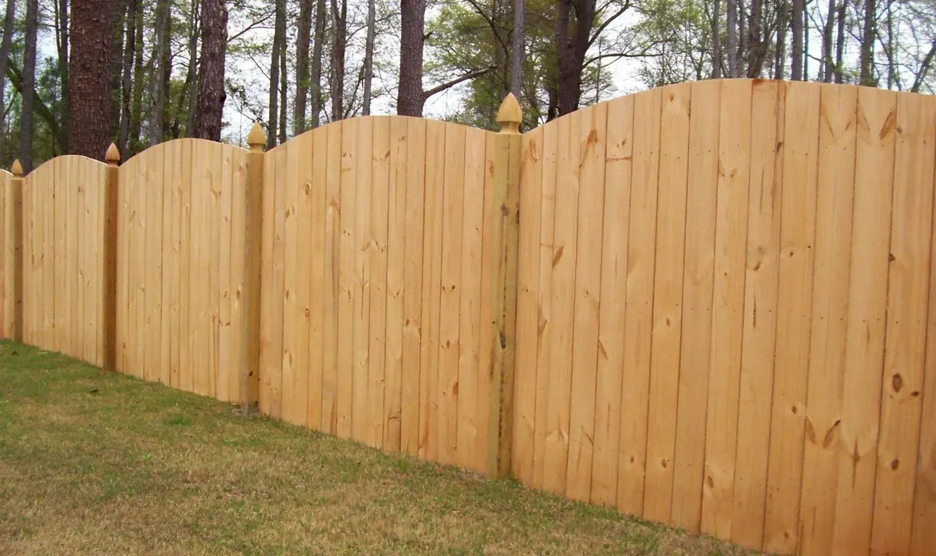 Wooden fence in a yard with grass and trees in the background.