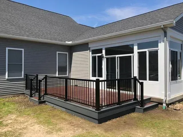 Deck with black railing next to a sunroom attached to a house with gray siding.