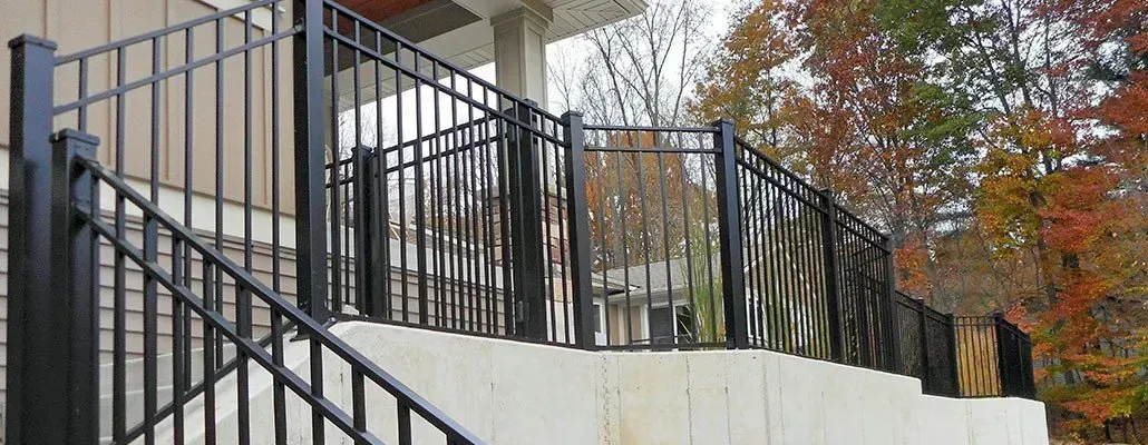 Black metal railing on a concrete structure with steps and a curved section. Trees in the background.