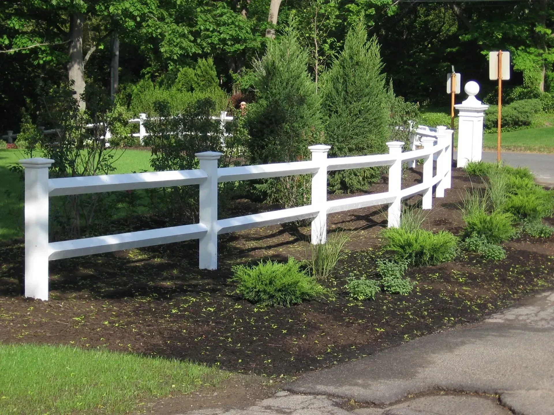 White picket fence curving along a landscaped area.