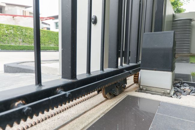 Sliding black metal gate with wheels and chain track, part of a residential entrance.