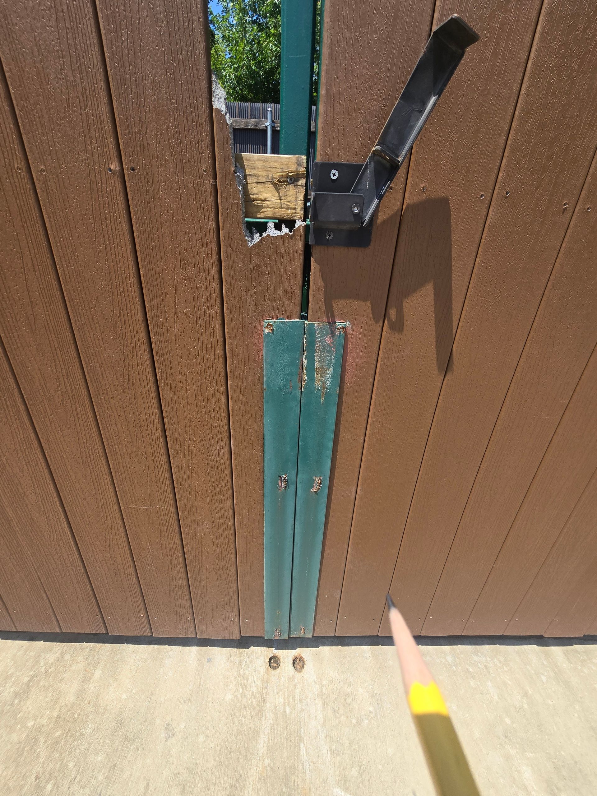 Brown wooden gate with a green vertical support; metal hardware and latch visible.