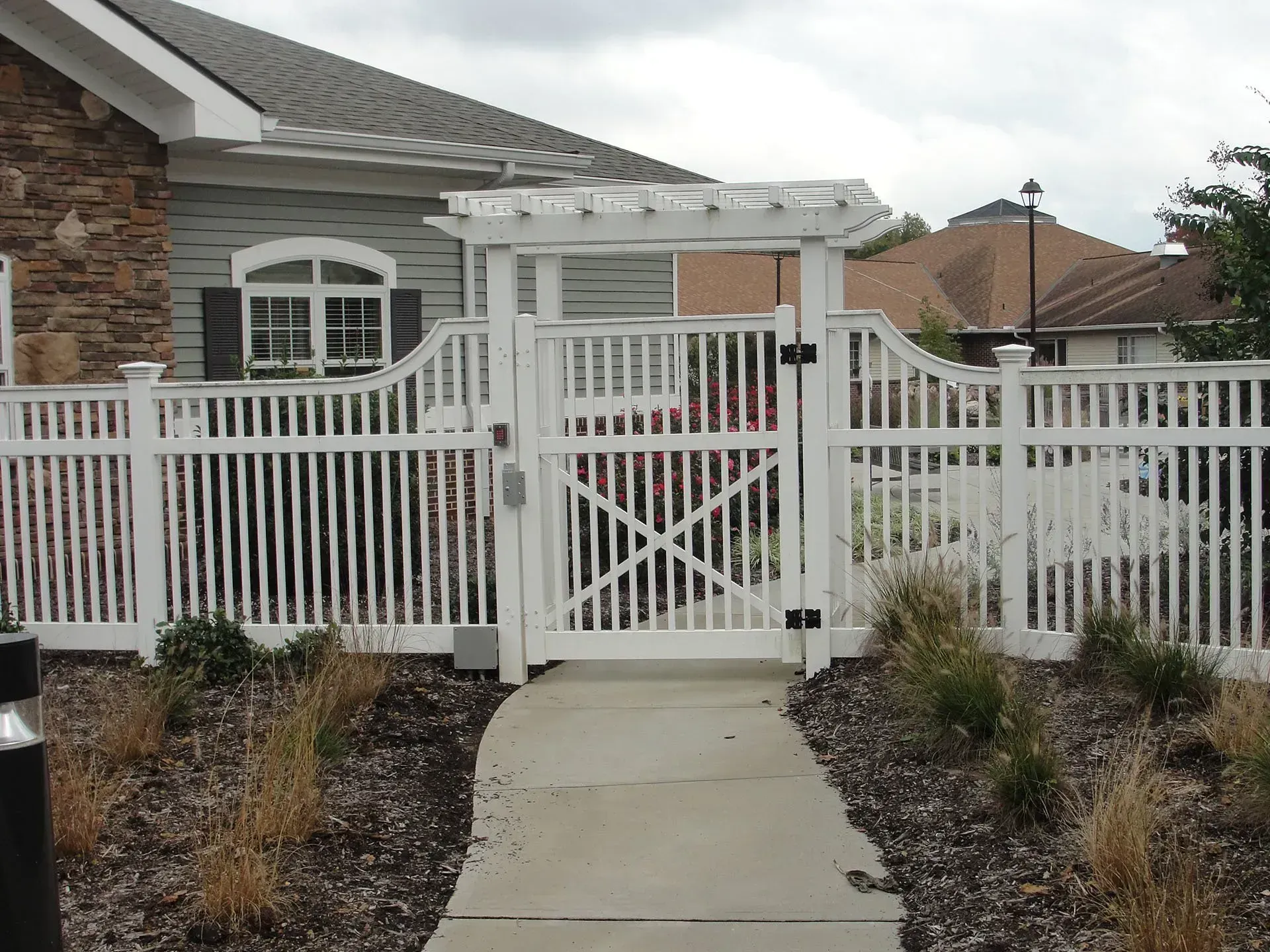 White picket fence with gate, leading to a pathway, with a building in the background.