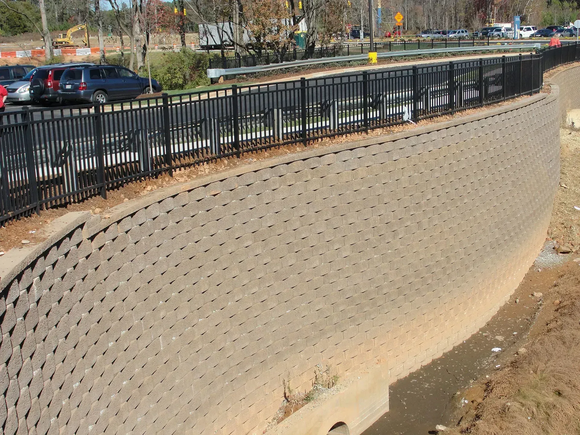 Concrete retaining wall with black metal railing. Cars and trees in the background.