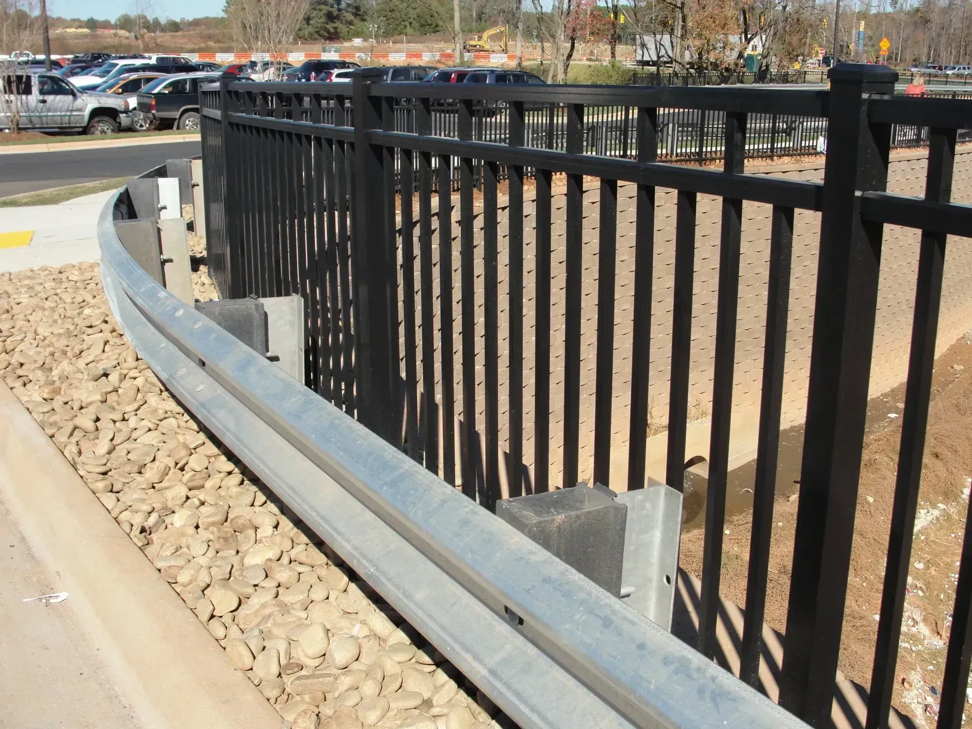 Black metal fence with guardrail next to a parking lot.