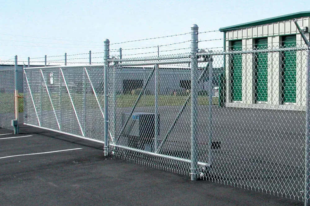 Chain-link fence with barbed wire on top, enclosing a paved area near industrial buildings.