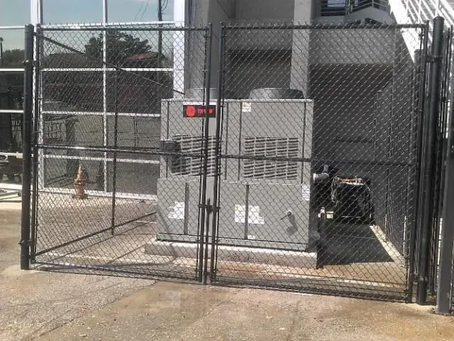 Black chain-link fence encloses two HVAC units, located outdoors next to a building.