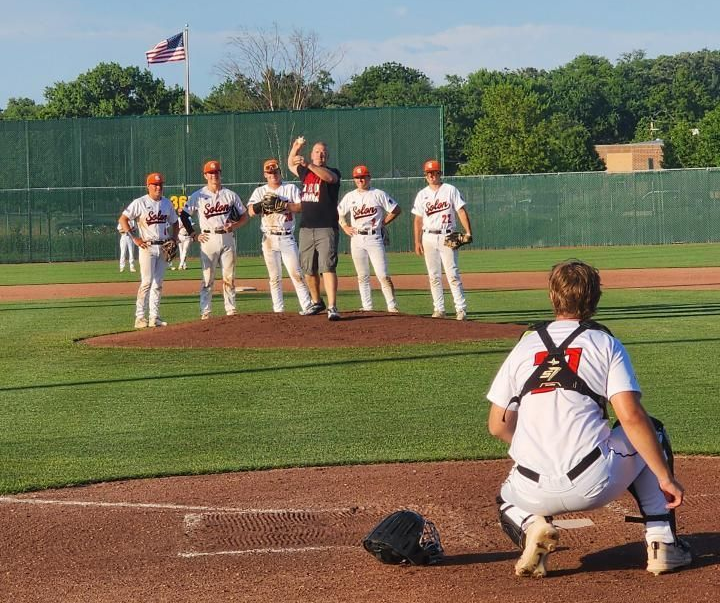 Baseball players on the field near home plate, with a catcher crouched in the foreground.