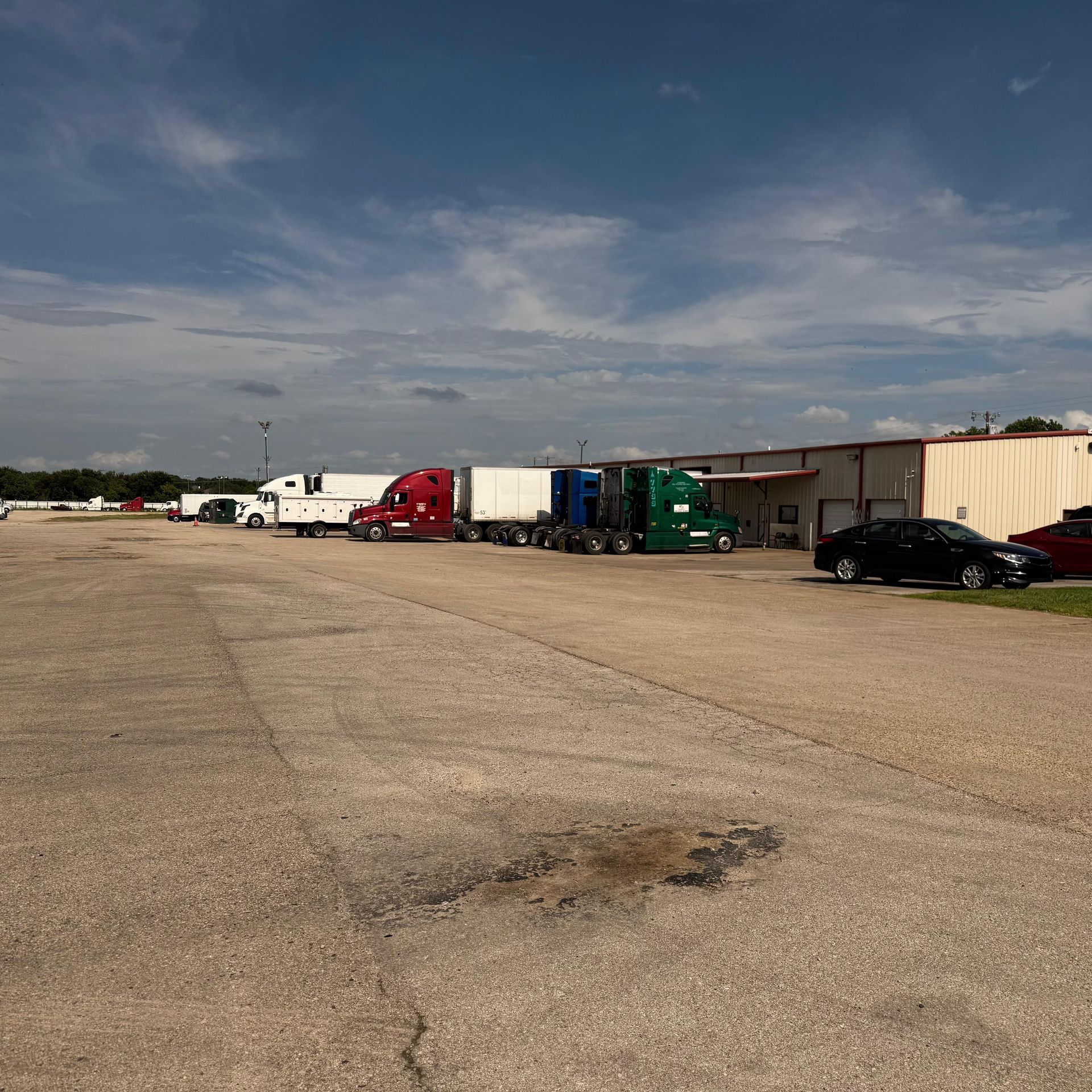 Semi-trucks parked at a loading dock on a paved lot under a cloudy sky.