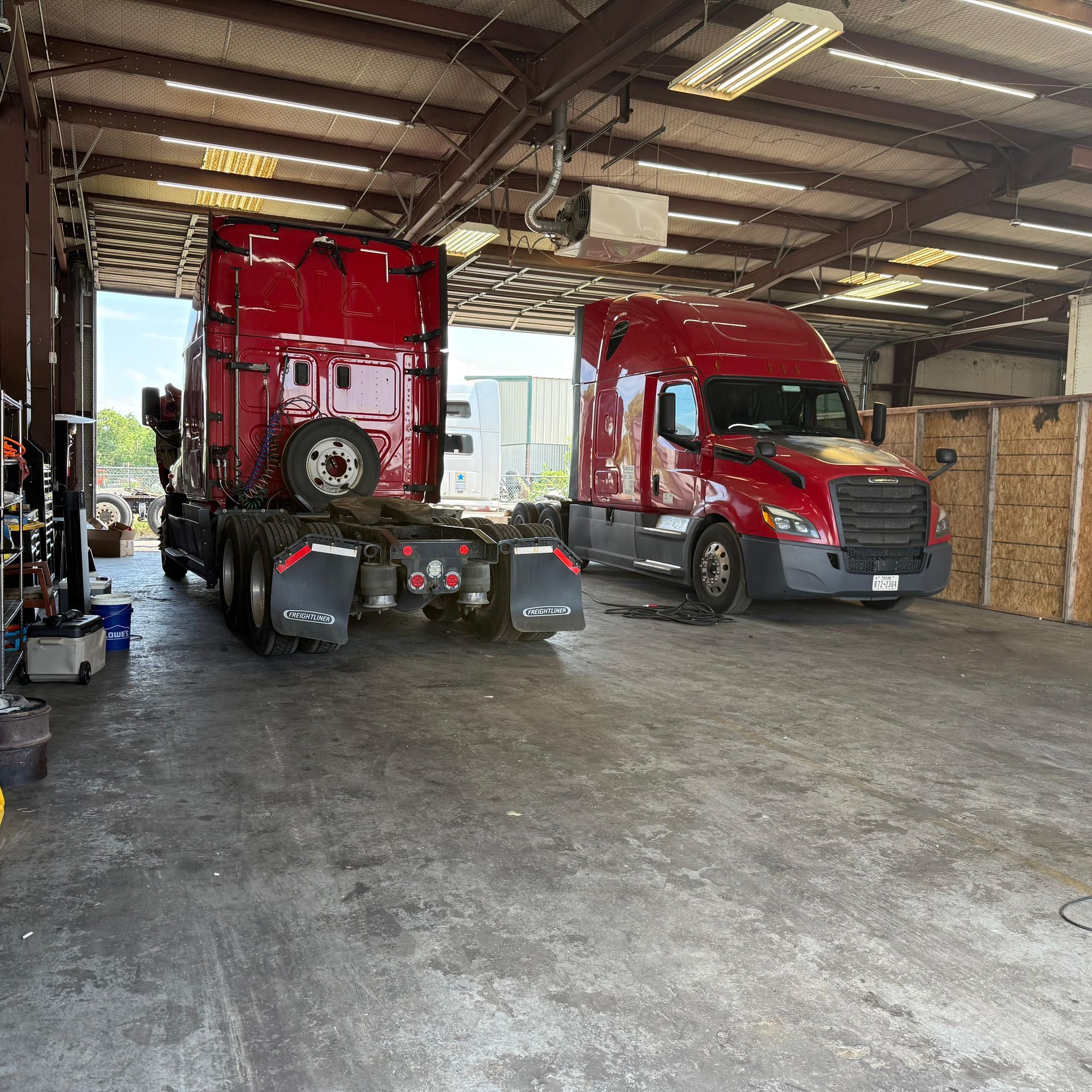 Two red semi-trucks parked inside a garage. One is facing backward, the other forward. Concrete floor.