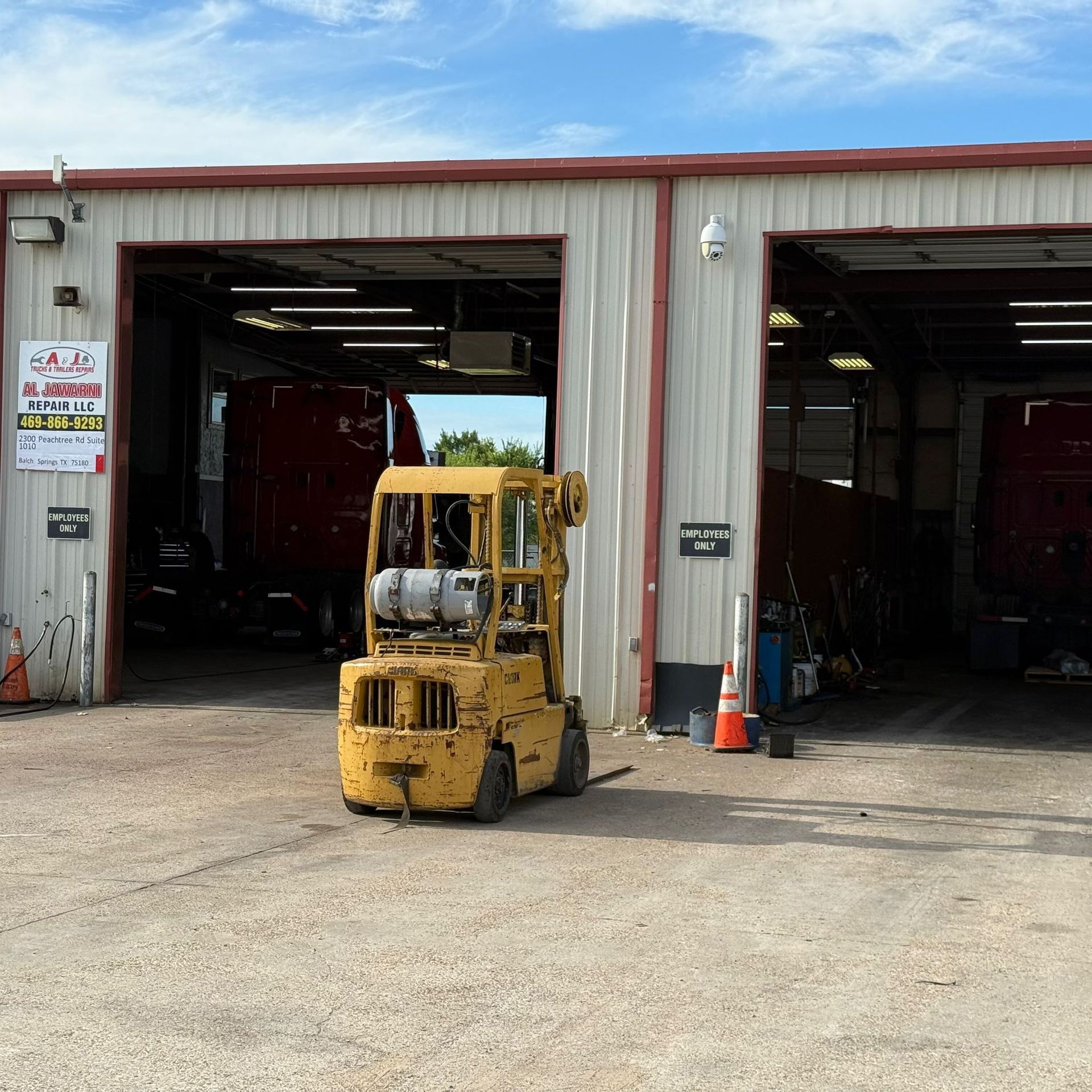 Yellow forklift parked in front of a garage with two open bays, red trucks visible inside.
