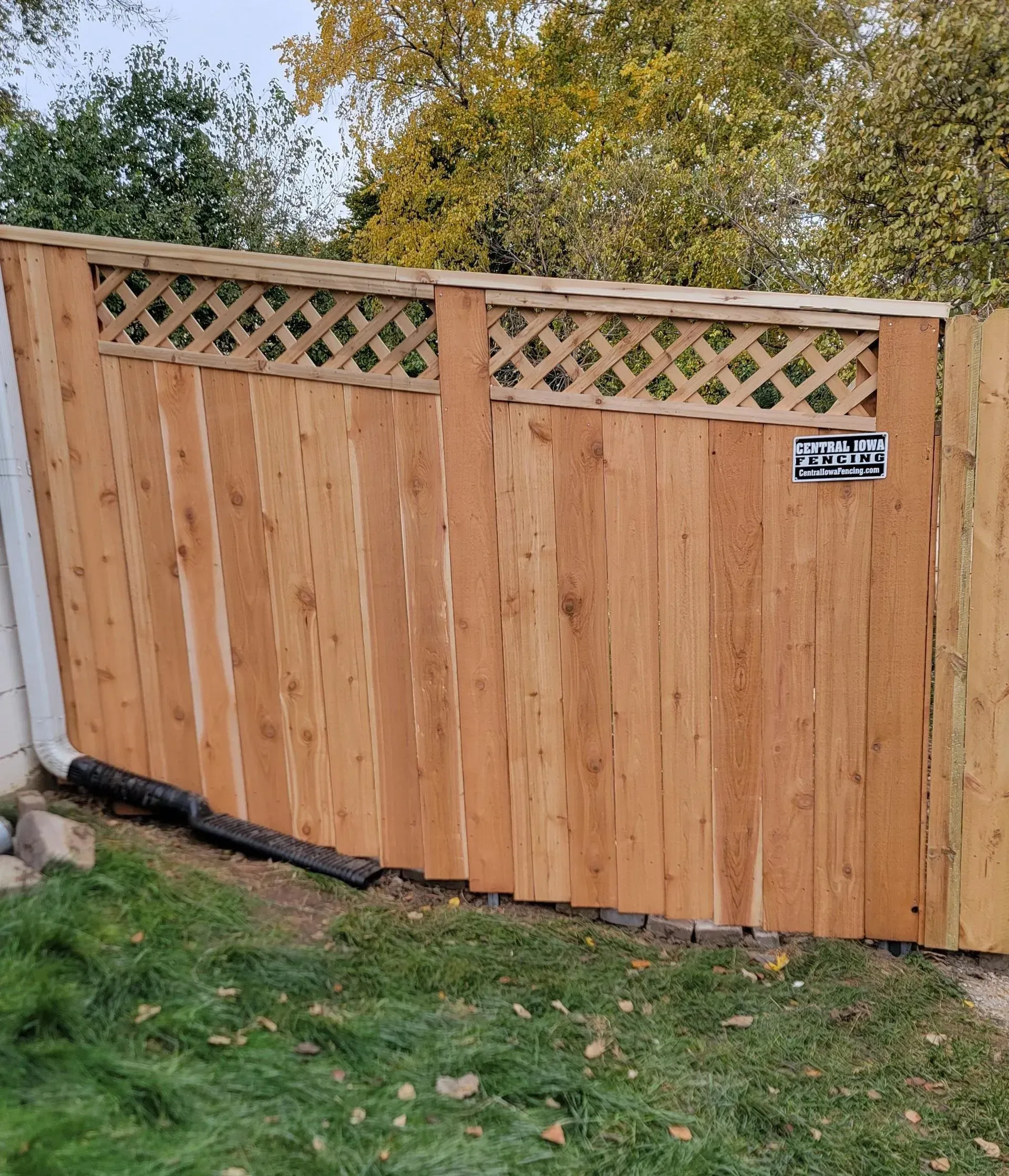 Wooden fence with lattice top, installed in a grassy yard, with a partly visible white wall.