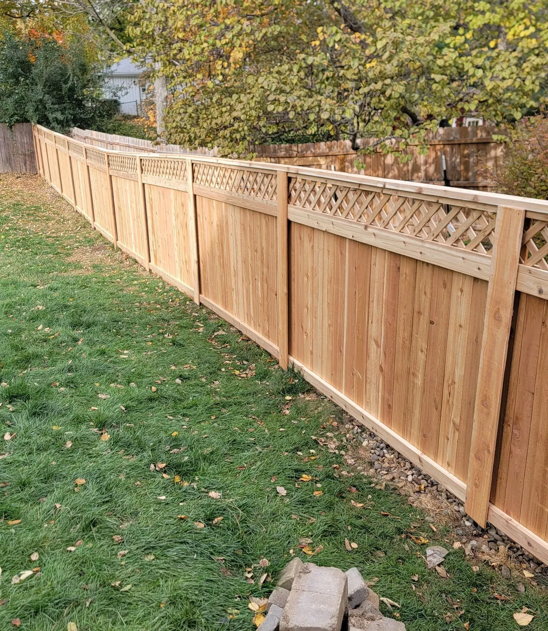 Wooden fence in a yard with grass and trees in the background.
