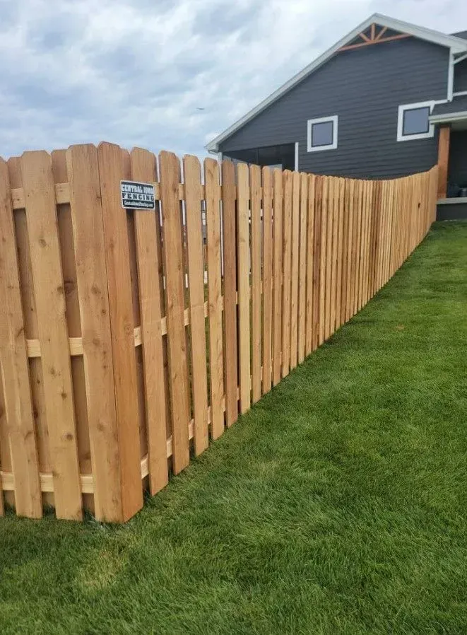 Wooden fence curving along a green lawn beside a dark-colored house on a cloudy day.