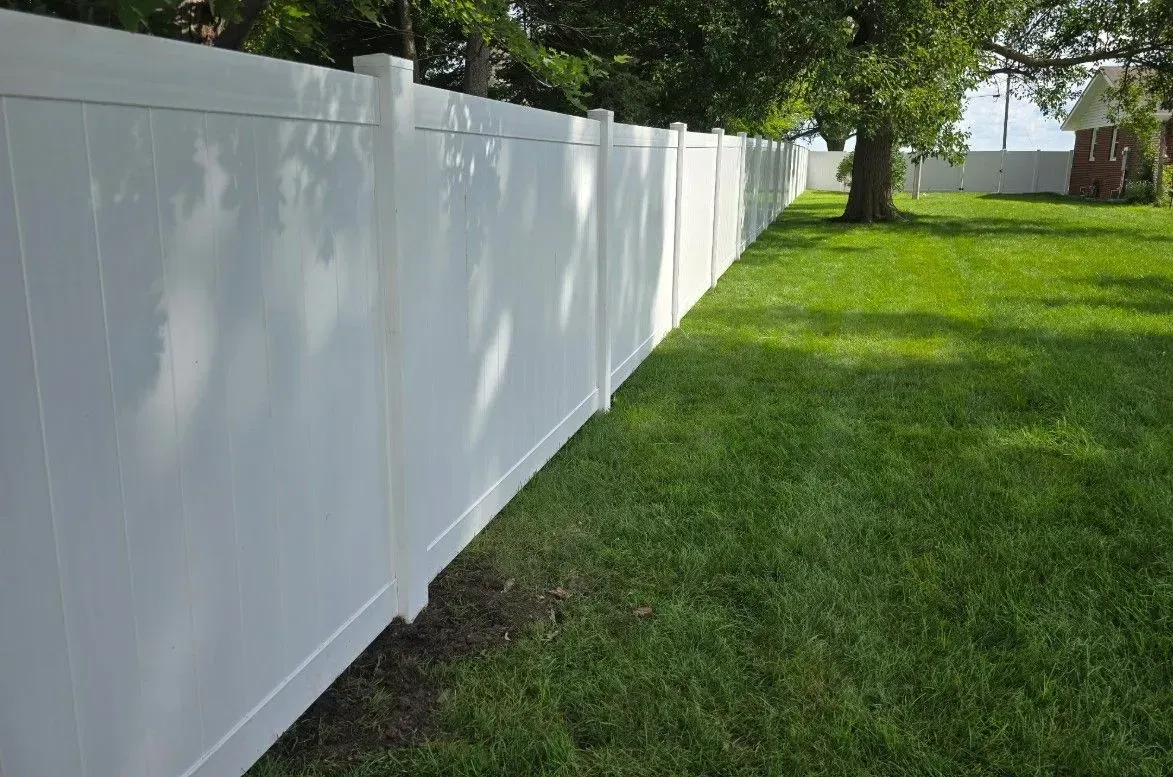White vinyl fence bordering a green lawn, under a bright sky.