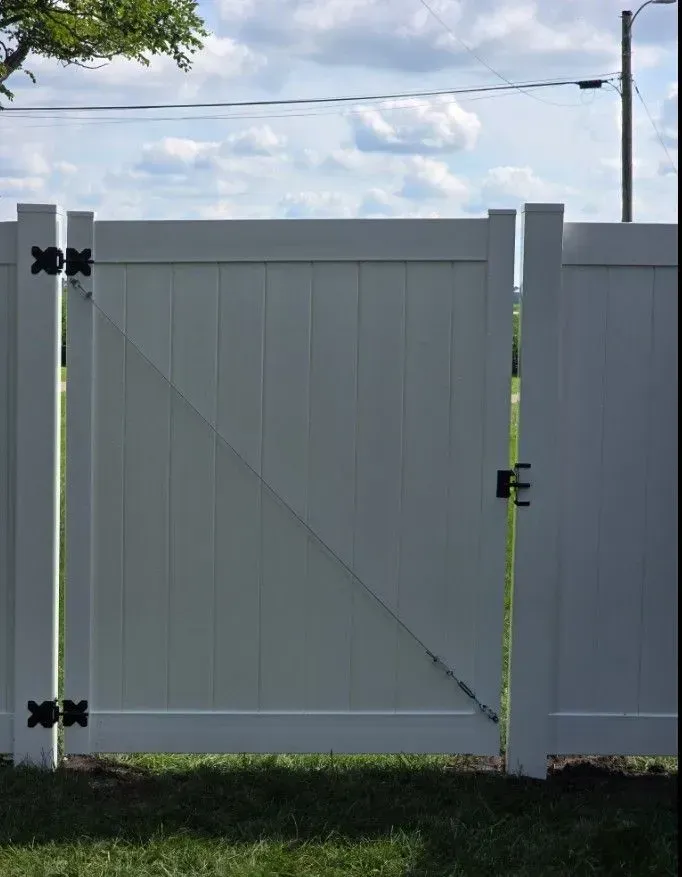 White vinyl fence gate with black hardware, open against blue sky.