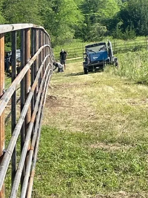 Rustic metal fence, path, and utility vehicle in a grassy field; two people nearby.