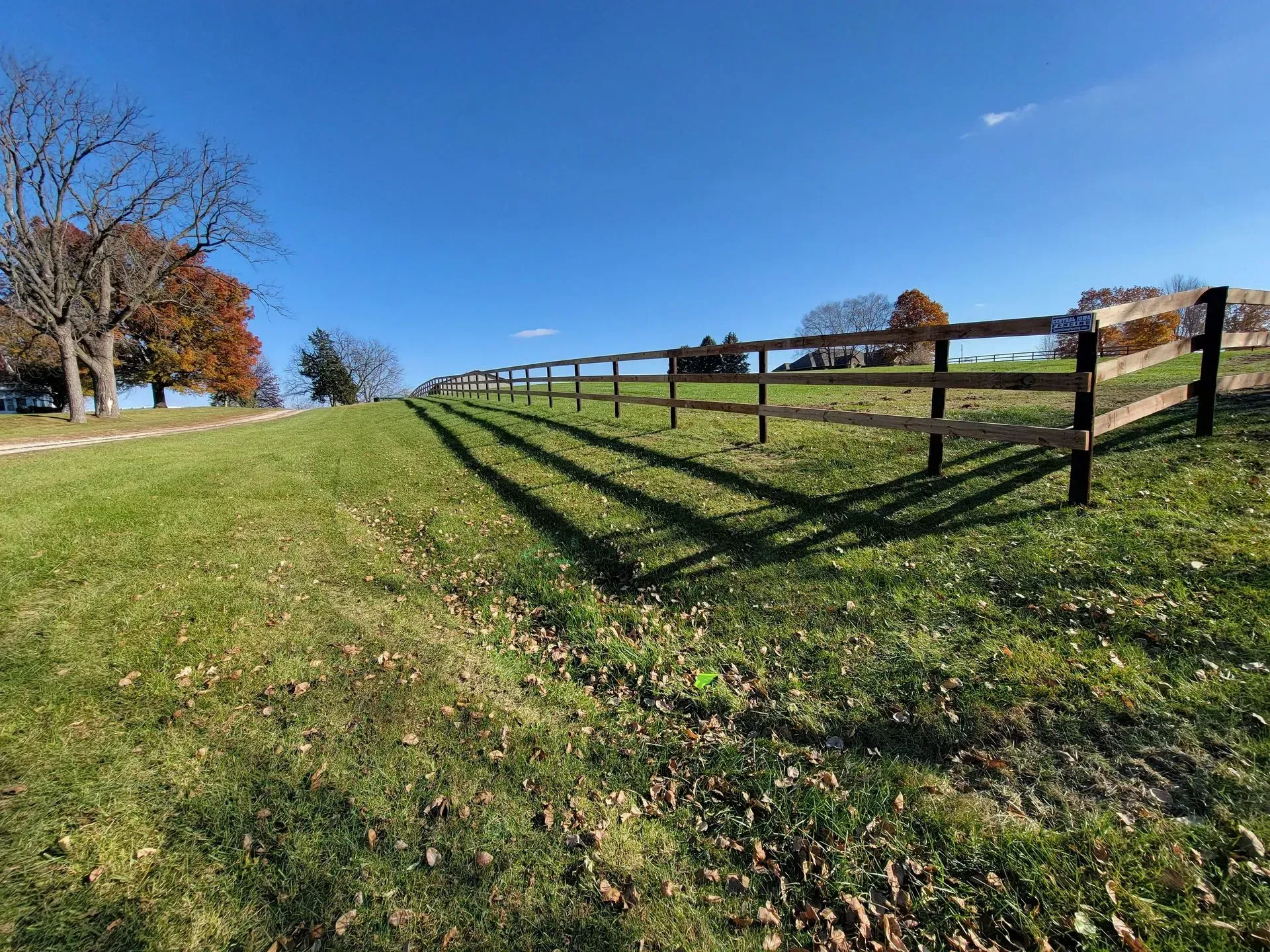 Wooden fence casting long shadows on a grassy hillside under a clear blue sky.
