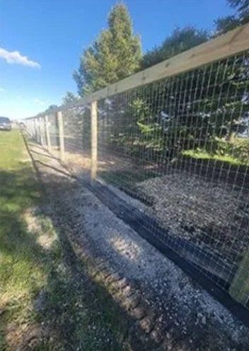 Wire fence with wooden posts and top rail, runs alongside a gravel path and grassy area under a blue sky.