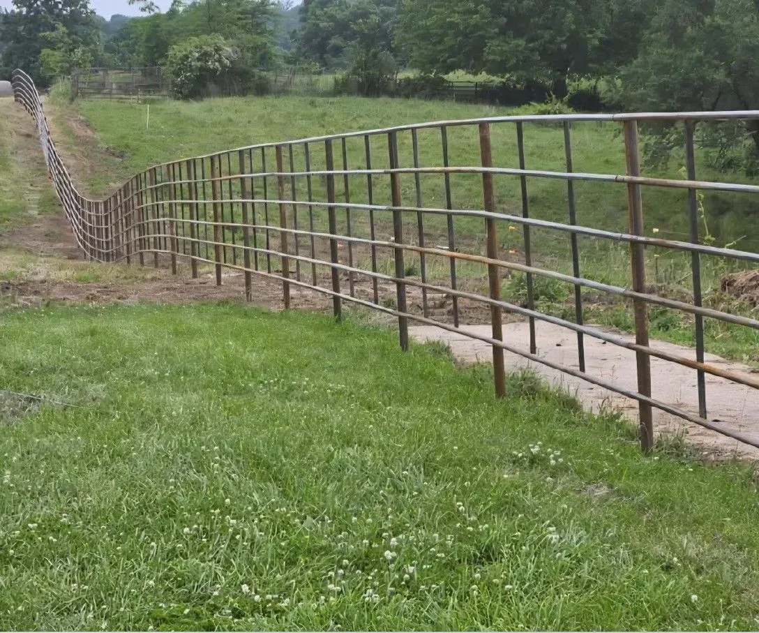 Metal fence along a grassy path, leading up a small hill in a green field.