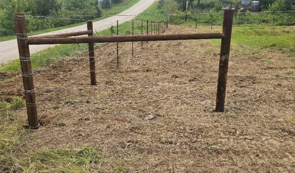 A metal fence structure with vertical posts and horizontal rails in a field.