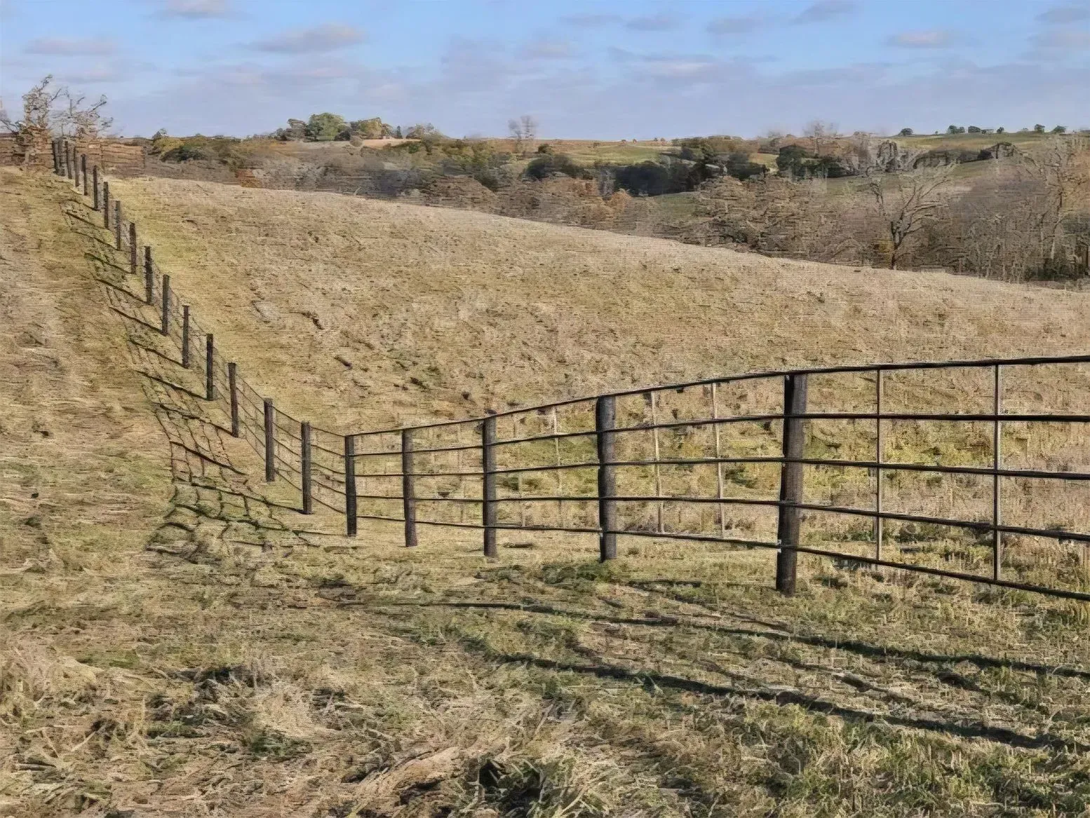 Metal fence lines a grassy hillside under a blue sky.