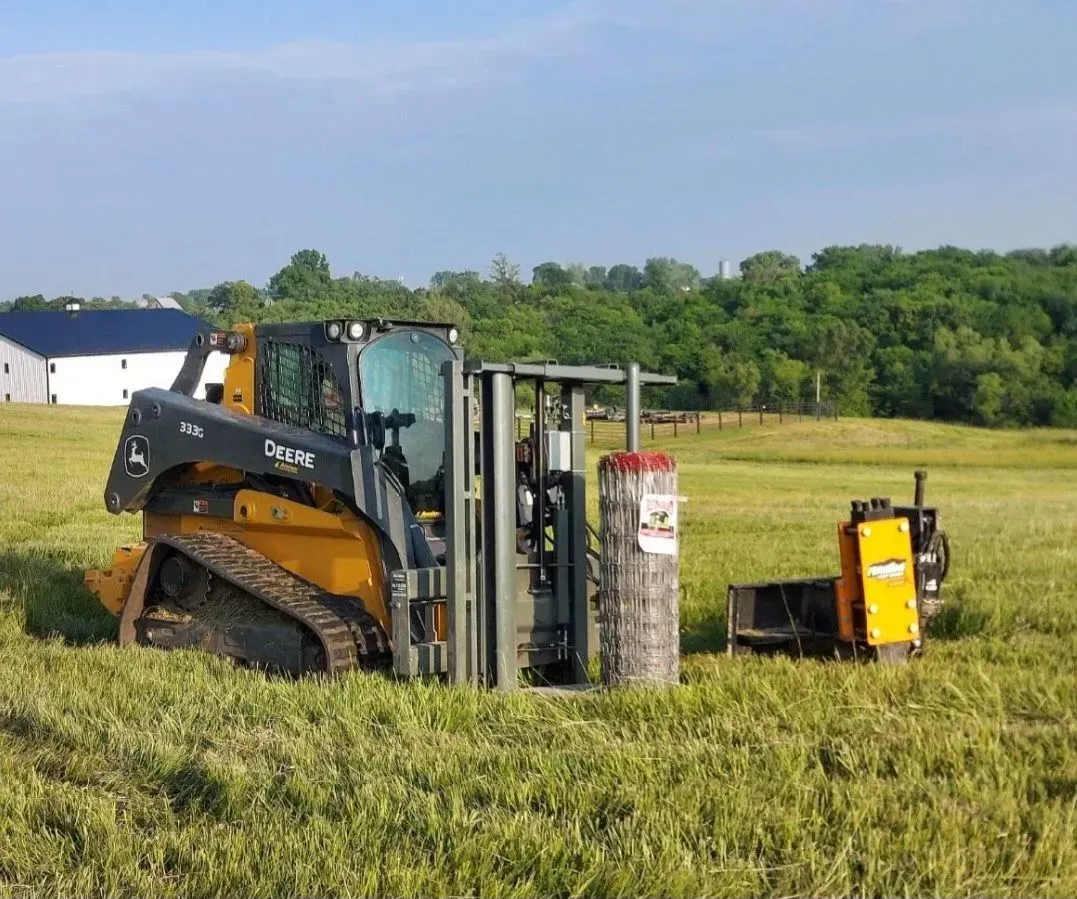Yellow skid steer with a bale handler in a field, holding a round bale.