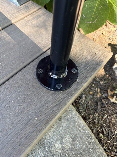 Black metal post base bolted to a wooden deck beside gravel and soil
