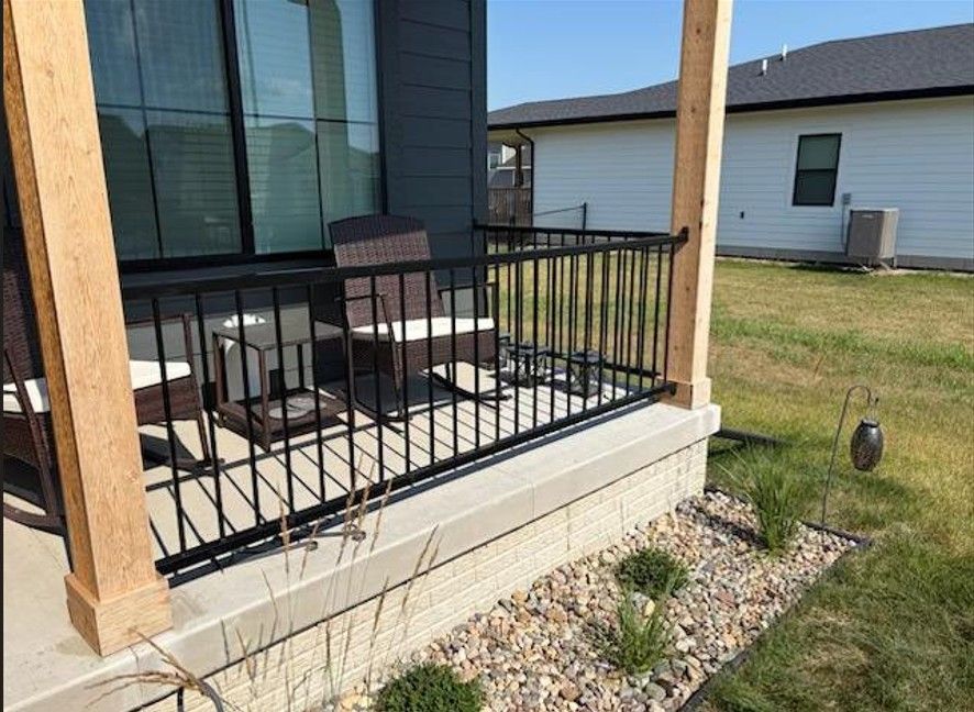 Patio with black metal railing, outdoor chairs, and gravel landscaping beside a house.