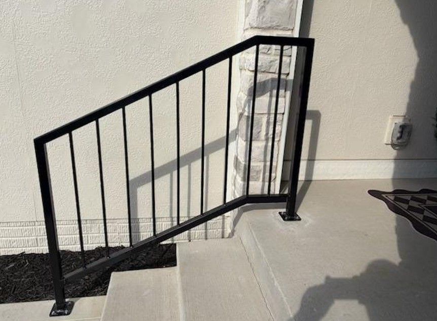 Black metal stair railing beside a white wall and column in a bright indoor space